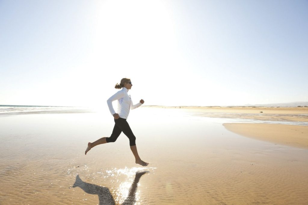 sporty woman jogging on wide sandy beach at bright sunshine